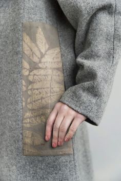 a person with their hand on the pocket of a coat that has a leaf print on it