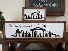 two framed nativity signs sitting on top of a wooden bench next to a christmas tree