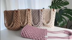 four crocheted bags sitting on top of a table next to a potted plant