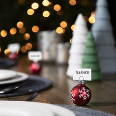 a table with place cards and christmas ornaments on it, along with plates and silverware