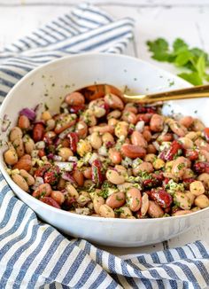 a white bowl filled with beans and garnish next to a blue striped napkin