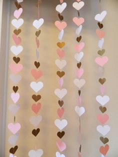 some paper hearts hanging from the side of a window with brown, pink and white colors