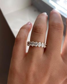 a woman's hand with a diamond ring on her left hand, in front of a window