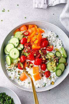 a white bowl filled with yogurt, cucumbers and tomatoes next to a spoon