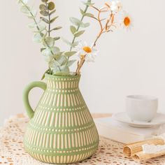 a green vase filled with flowers sitting on top of a table next to a cup