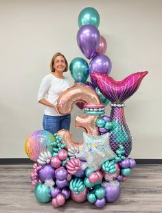 a woman standing next to a large number balloon sculpture in the shape of a mermaid