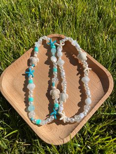 two bracelets with seashells on them sitting in the grass next to a wooden tray