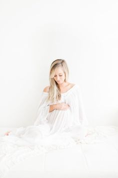 a woman sitting on top of a bed with her arms around her chest and eyes closed