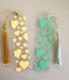 two bookmarks with hearts and tassels attached to each other on a table