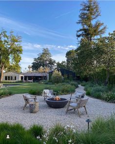 an outdoor fire pit in the middle of a gravel area surrounded by trees and bushes