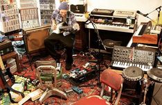 a man sitting on top of a chair in a room filled with musical instruments and keyboards