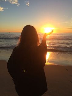 a woman standing on top of a beach next to the ocean holding her hand up