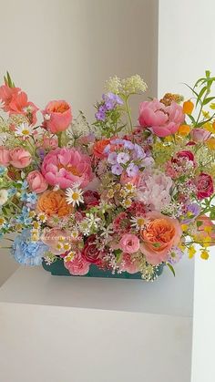 a vase filled with lots of colorful flowers on top of a white shelf next to a wall