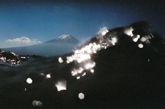 some paper lanterns floating in the air over a mountain range at night with snow capped mountains in the background