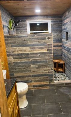 a bathroom with stone walls and flooring in the shower area, along with a television mounted on the wall