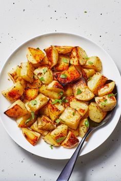 a white plate topped with cooked potatoes on top of a table next to a fork