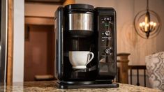 a black coffee maker sitting on top of a counter next to a cup and saucer