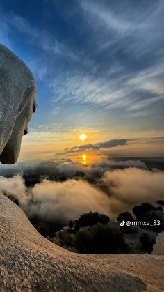 the sun is setting over some clouds and mountains in the distance, with a statue on top