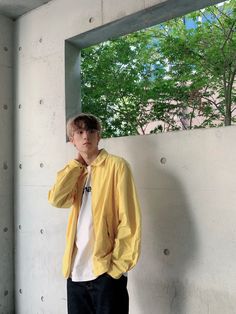 a man standing in front of a window with his hand on his face and wearing a yellow jacket