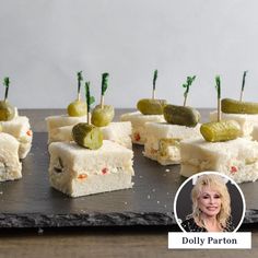 small sandwiches with pickles on them sitting on a slate platter next to a woman's face