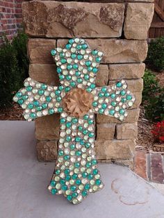 a decorative cross made out of beads on a stone wall in front of a brick building