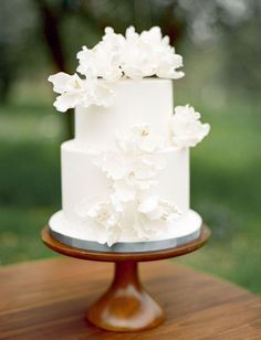 a wedding cake with white flowers on top sits on a table in front of the grass