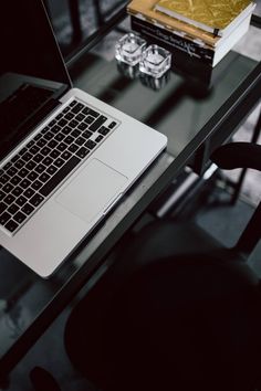 an open laptop computer sitting on top of a glass table next to a book and chair