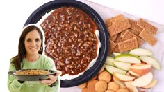 a woman holding a plate with baked beans and crackers next to a platter of food