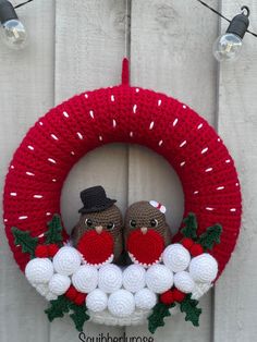 two knitted owls sitting on top of a christmas wreath hanging from a white fence