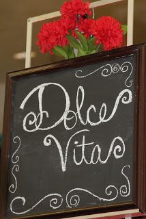 a chalkboard sign that says dolce vita with red carnations in the background