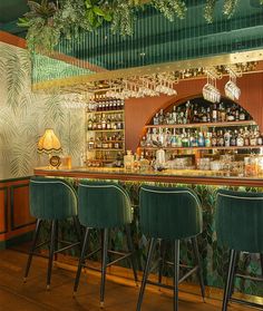 the bar is decorated with green velvet chairs and greenery hanging from the ceiling above it