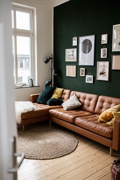 a brown leather couch sitting in front of a green wall with pictures on the wall