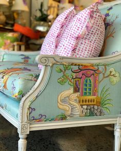 an upholstered chair with a pink and blue pillow on it's back