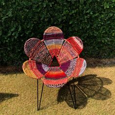 a chair made out of yarn sitting on top of a grass covered field next to a bush