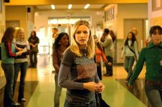 a group of people standing in a hallway with one woman looking at the camera and two men walking behind her