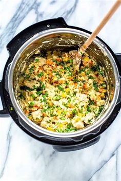 a pot filled with rice and vegetables on top of a marble countertop next to a wooden spoon