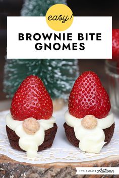 two brownie bites with white frosting and strawberries on top, sitting next to a small christmas tree