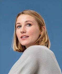 a woman with blonde hair and blue eyes looks up at the camera while wearing a white top