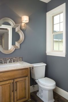 a white toilet sitting under a bathroom mirror next to a sink with a wooden cabinet