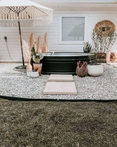 an outdoor hot tub surrounded by rocks and plants in front of a white house with a large umbrella over it