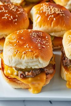 several cheeseburgers on a white plate with sesame seeds