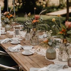 a long wooden table topped with plates and vases filled with flowers