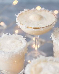 three glasses filled with drinks sitting next to each other on top of a table covered in lights