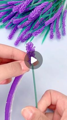 someone is making a flower out of plastic straws and purple flowers are in the background