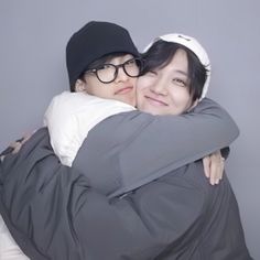 two people hugging each other in front of a gray wall