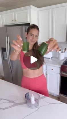 a woman in a pink top is holding up some green leaves to her face while standing at the kitchen counter