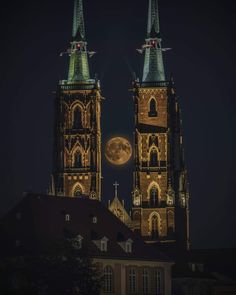 the moon is setting behind two tall buildings with spires on top, in front of a dark night sky