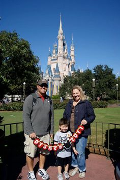 two adults and a child standing in front of a castle