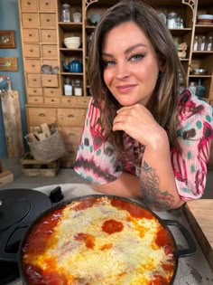 a woman sitting at a table with a pizza in front of her on the stove