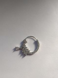 a pair of silver hoop earrings on a white surface with one earring in the shape of a leaf